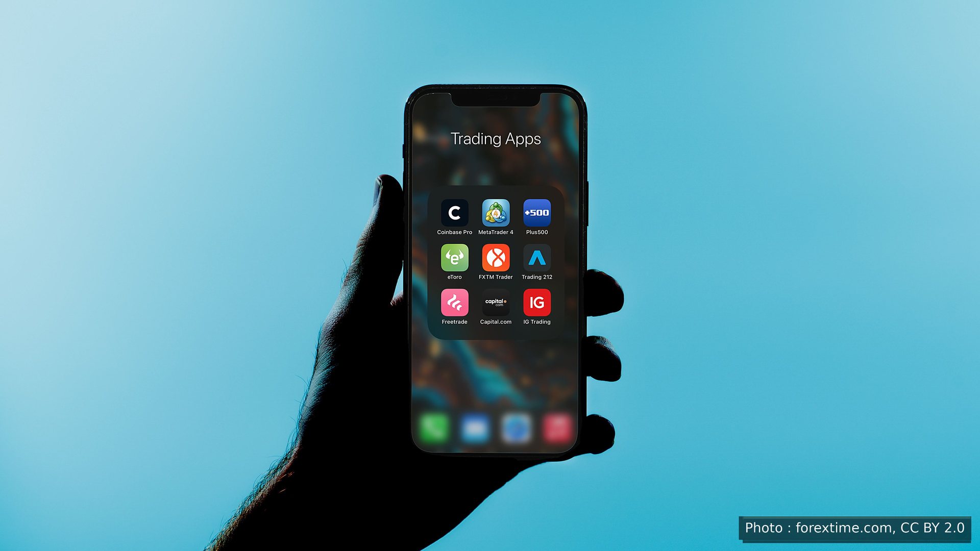 Une main tenant un téléphone rempli d’applications de trading, en silhouette