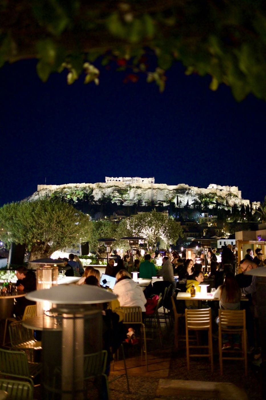 Un restaurant sur un toit la nuit, sous l'Acropole illuminée, à Athènes
