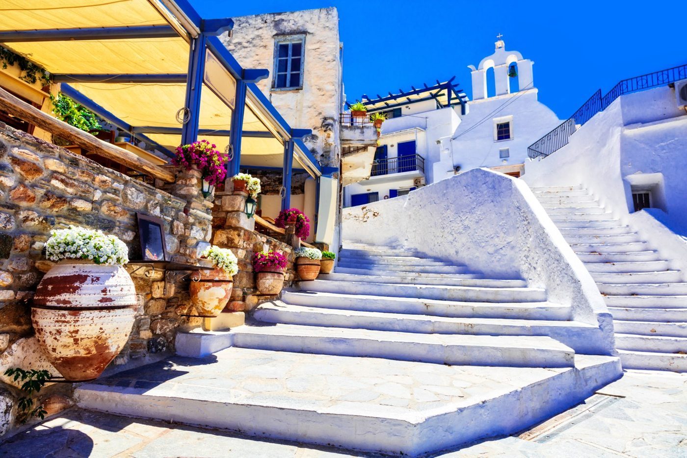 Escaliers blanchis à la chaux, fleurs et chapelle au dôme bleu dans un village de Naxos